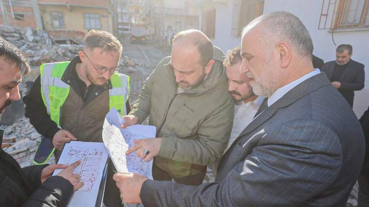 Yıkım alanında, belgeleri inceleyen beş kişi, çevrede molozlar var.