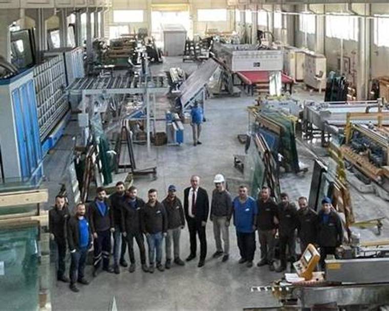 Metal işleme atölyesinde, çeşitli makinelerin önünde yan yana duran bir grup çalışan görülüyor.