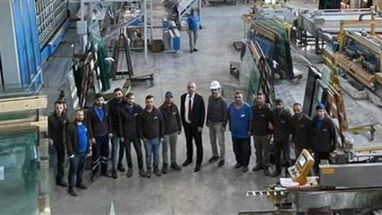 Metal işleme atölyesinde, çeşitli makinelerin önünde yan yana duran bir grup çalışan görülüyor.