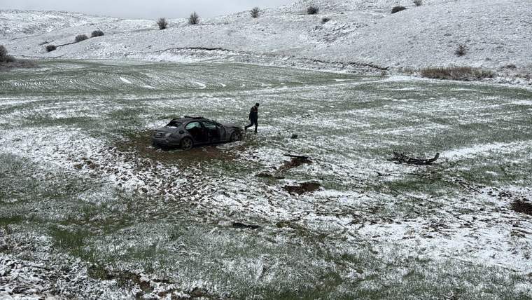 Karla kaplı arazide devrilmiş bir araç ve yanında bir kişi duruyor.