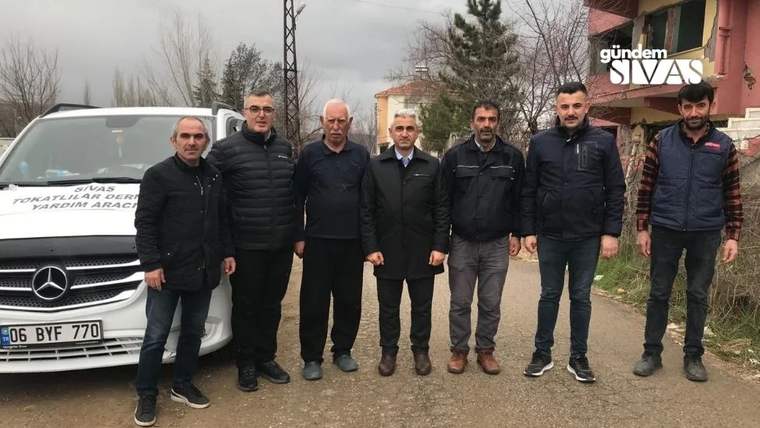 Yedi kişi, üzerinde yazılar bulunan beyaz minibüsün önünde dışarıda yan yana duruyor.