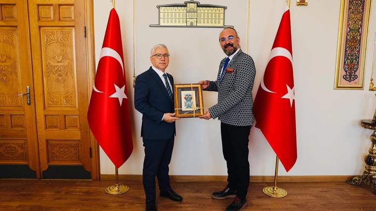 İki kişi, Sivas Valiliği önünde bir tabloyu takdim ediyor. Arkada Türk bayrakları var.
