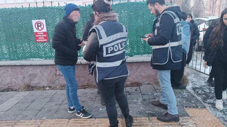 Polis yazılı yelek giyen iki kişi, kaldırımda başka bir kişiyle konuşuyor; çevrede yayalar bulunuyor.