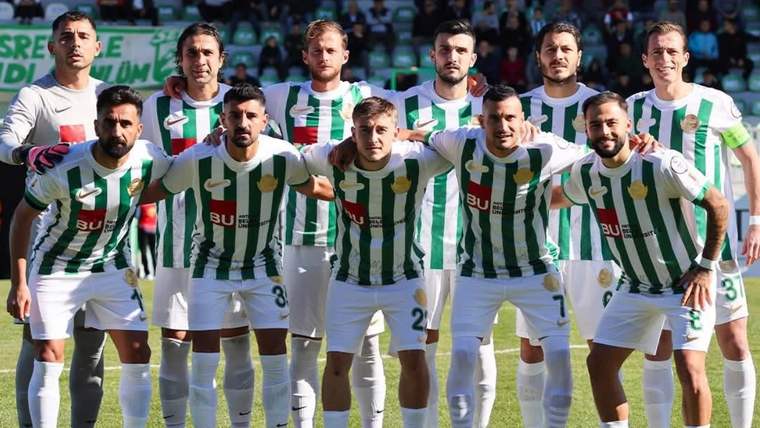 Yeşil beyaz çubuklu formalı futbolcular, saha üzerinde takım halinde yan yana durarak poz veriyor.