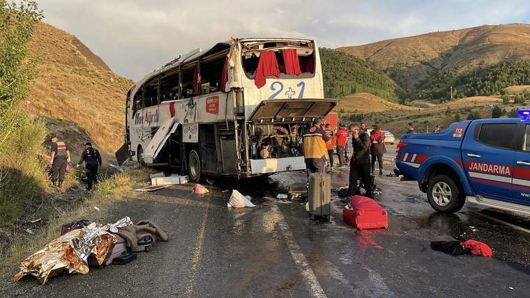 Dağlık yoldaki ağır hasarlı otobüsün çevresinde insanlar ve jandarma aracı, yola saçılmış eşyalar görülüyor.