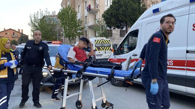 Polislerin yanında sedyede taşınan yaralı bir genç ve arkasında bekleyen ambulans görülüyor.