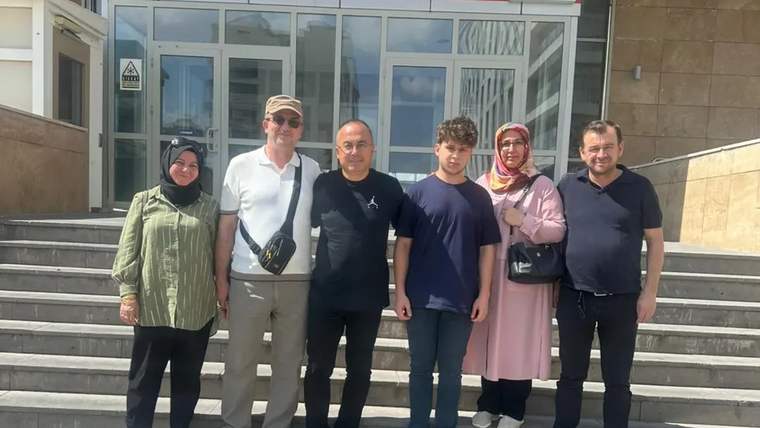İdari bina girişindeki merdivenlerde, beş yetişkin ve bir genç yan yana duruyor.