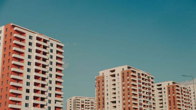 Açık mavi gökyüzü altında, farklı yüksekliklerde çok katlı apartman blokları görülüyor.