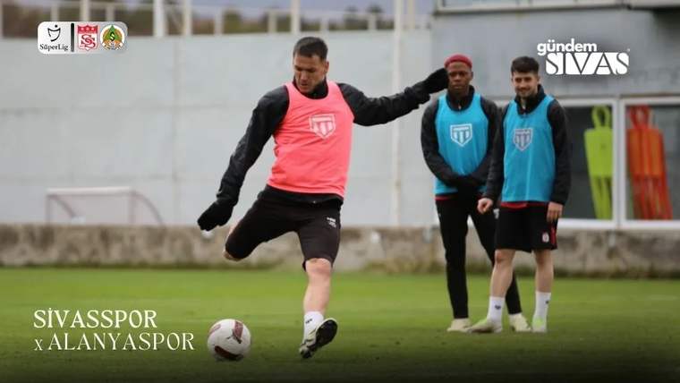 Antrenman sahasında pembe yelek giymiş bir futbolcu, topa vurmak üzere hazırlanıyor; arka planda iki oyuncu bekliyor.