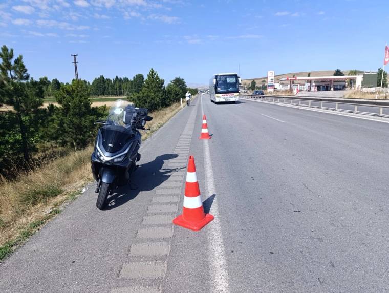 Yol kenarında devrilmiş bir motosiklet ve trafik konileri, ileride seyir halinde bir otobüs görülüyor.