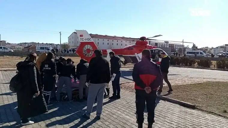 Helikopterin yanında, sağlık ekipleri ve kalabalık bir grup, sedye ile bir kişiyi taşıyor.