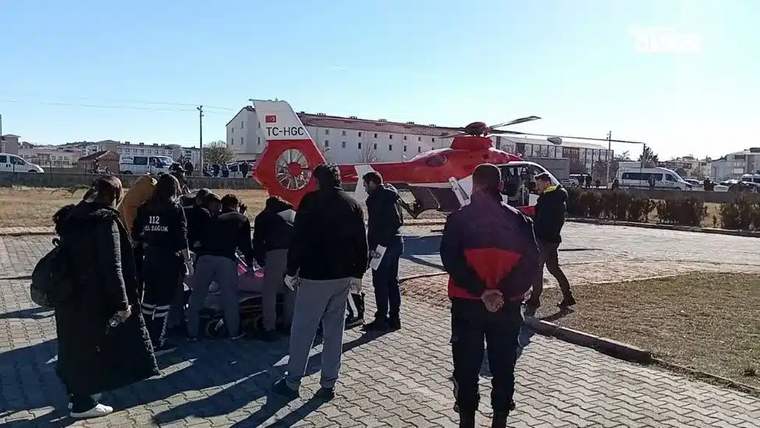 Helikopterin yanında, sağlık ekipleri ve kalabalık bir grup, sedye ile bir kişiyi taşıyor.