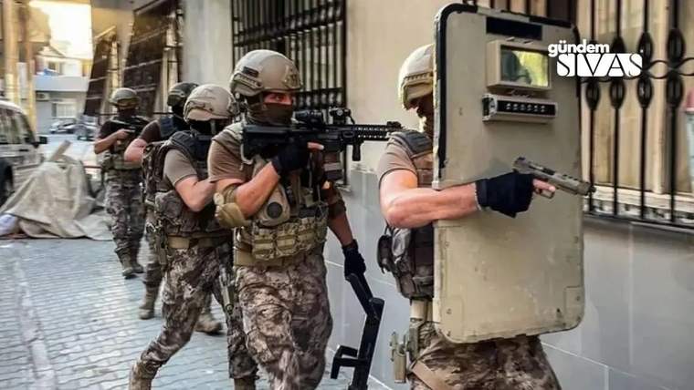 Askeri kıyafet giymiş dört kişi, bir sokakta ilerliyor; biri kalkan tutuyor, diğeri tüfek taşıyor.