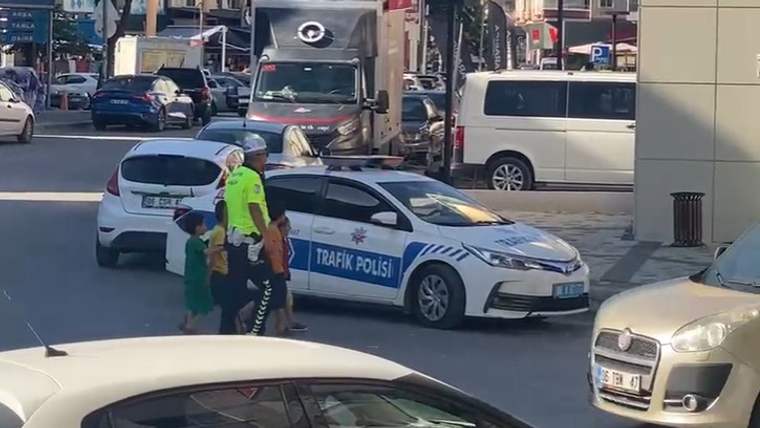 Trafik polisi üniformalı bir kişi, dört çocuğun ellerinden tutarak caddede ilerliyor.