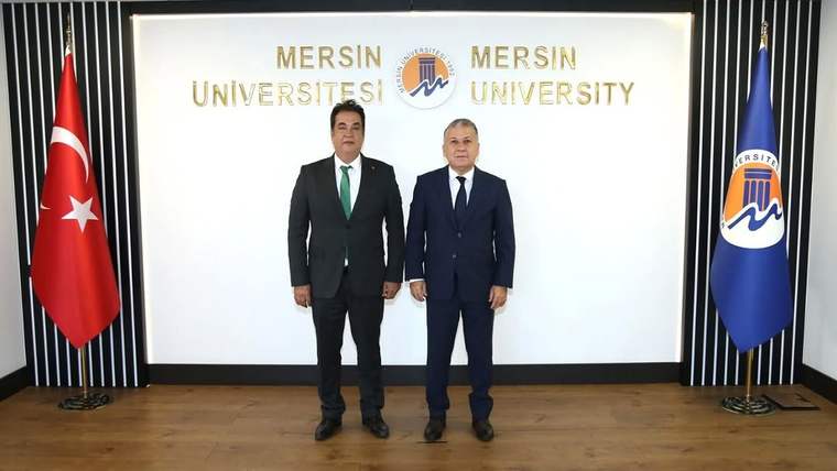 Mersin Üniversitesi logosunun bulunduğu arka planda, iki kişi yan yana duruyor.
