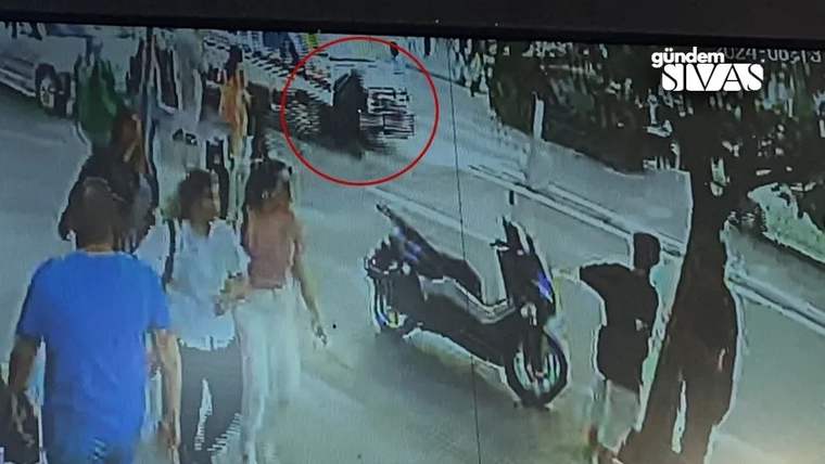 Güvenlik kamerası görüntüsünde, yaya ve ambulansın bulunduğu bir sokak görünmekte.
