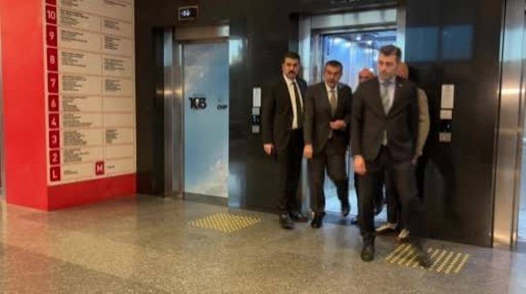 Asansörlerin önünde takım elbiseli dört erkekten biri önde yürürken diğerleri arkasından ilerliyor.