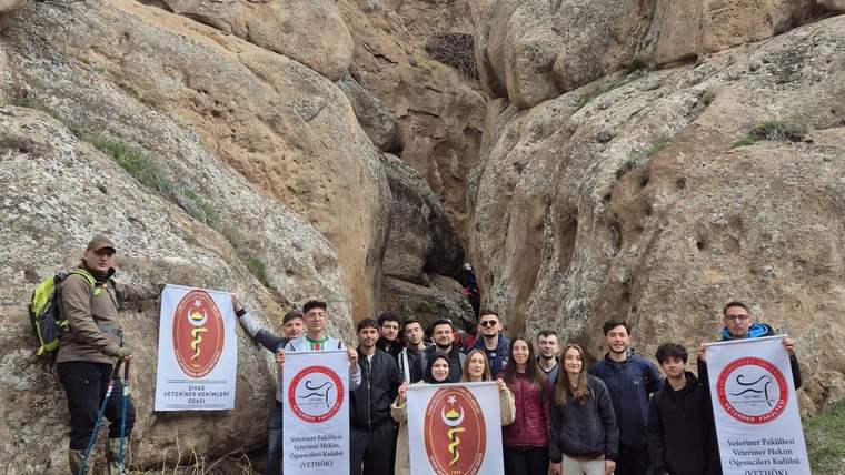 Kayalık bir geçitte kalabalık bir grup, üzerinde veterinerlik sembolleri bulunan pankartlarla yan yana duruyor.