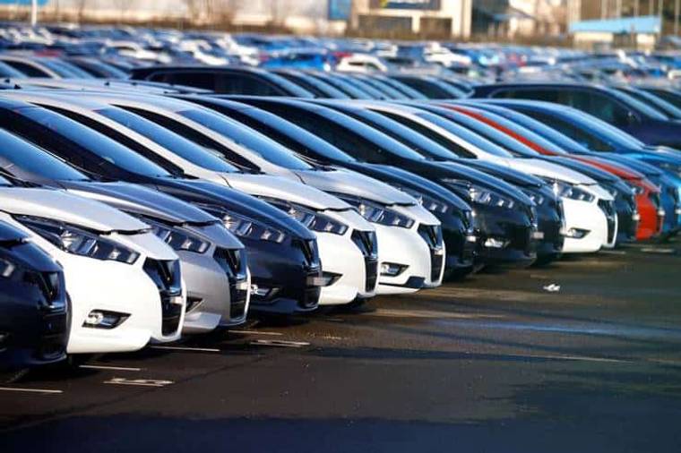 Bir otoparkta sıralanmış farklı renklerde araçlar, çoğunlukla gri ve beyaz tonlarında.