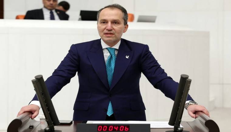Kürsüde duran takım elbiseli bir kişi, iki mikrofonun arasında ellerini kürsüye koyuyor.