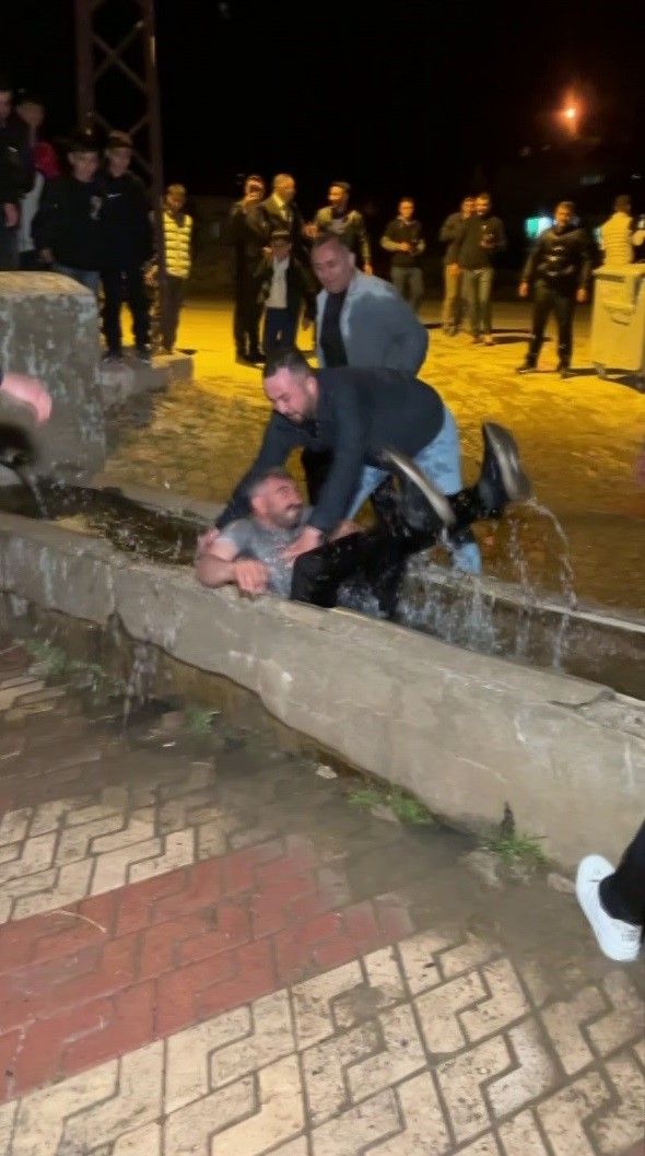 Gece çekiminde, beton su kanalında oturan bir adamın yanında eğilen başka bir adam ve akan su görülüyor.