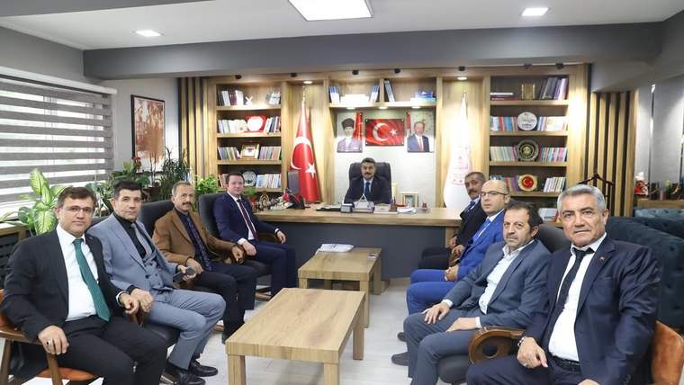 Makam odasında, kitaplık ve Türk bayrağı önünde oturan dokuz kişi ile bir masa görülüyor.