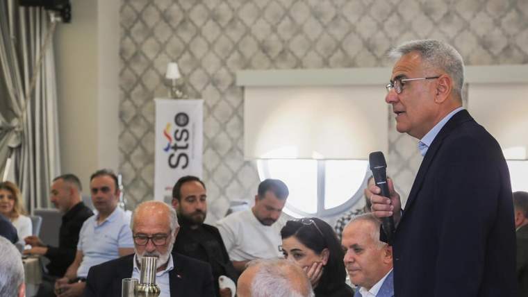 STSO yazılı panonun bulunduğu salonda, elinde mikrofon tutan bir kişi konuşurken katılımcılar oturuyor.