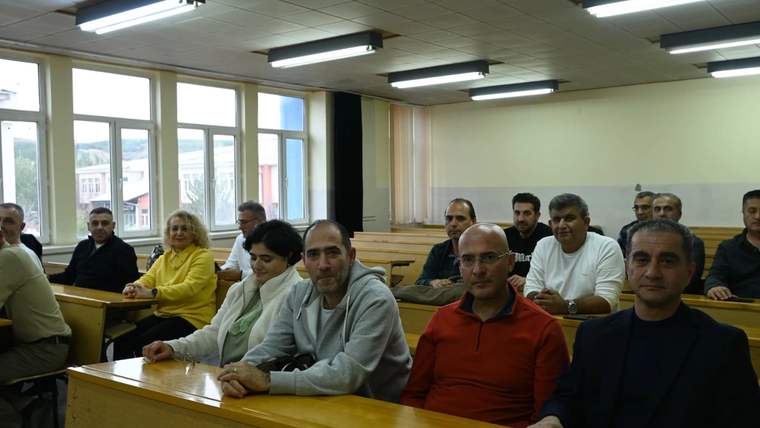 Sınıf ortamında oturan mezunlar, ön sırada dört kişi dikkatlice poz veriyor.