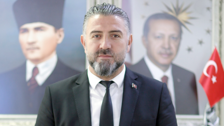 Fatih Deveci, arkasında Atatürk ve Erdoğan'ın portreleriyle birlikte, resmi bir kıyafetle poz veriyor.