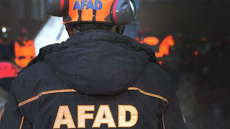 AFAD yazılı mont giymiş bir kişi, arka planda başka kişilerin silüetleri görünmekte.