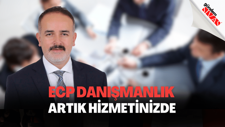 Takım elbiseli, bıyıklı bir kişi; masadaki kişilerin ve büyük tanıtım yazısının önünde duruyor.