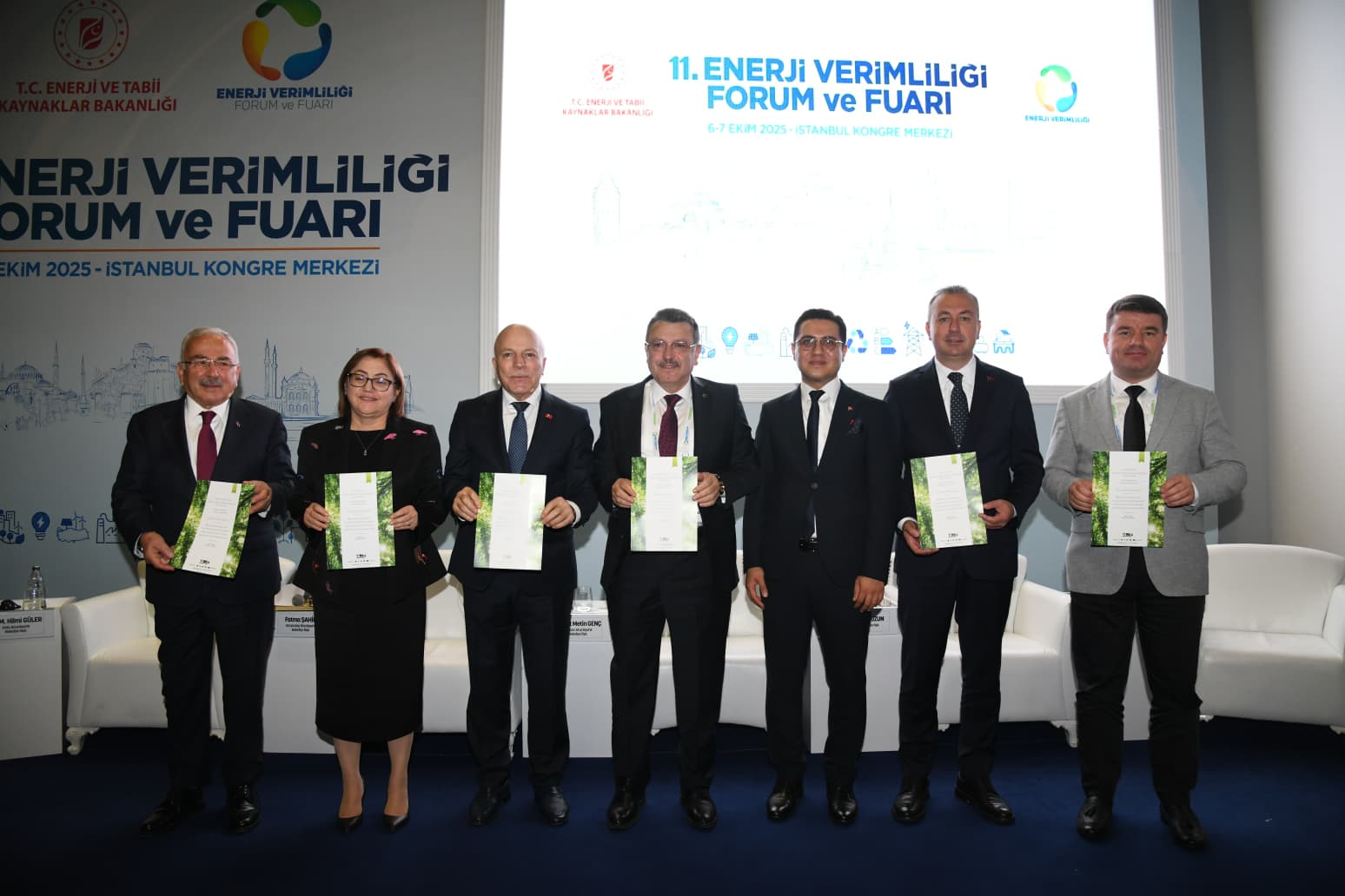 Enerji Verimliliği Forumunda, belgelerle poz veren altı kişi, arka planda etkinlik afişi var.