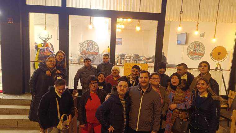 Aydınlatılmış bir işletmenin girişinde, merdivenlerde ve kapı önünde kalabalık bir grup birlikte duruyor.