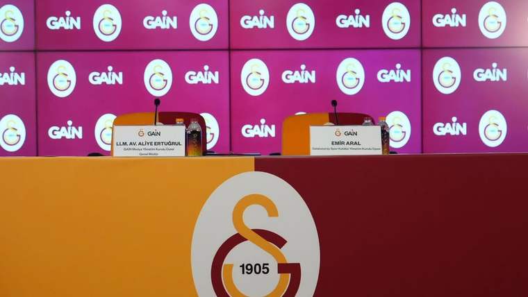 Galatasaray logosu ve GAIN yazılarıyla kaplı fonda, iki isimlikli basın toplantısı masası görülüyor.