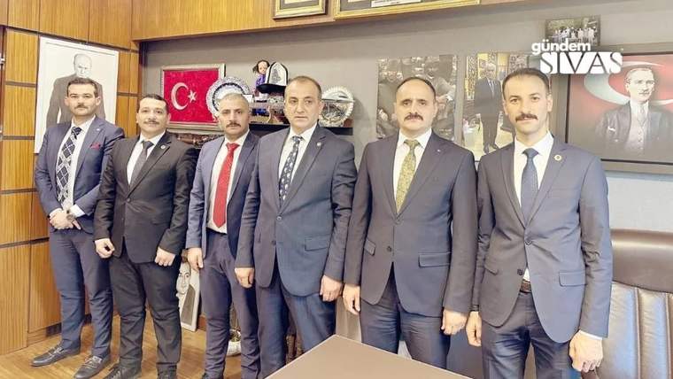 Altı kişi, bir ofiste yan yana duruyor; arka planda Türk bayrağı ve çeşitli ödüller var.