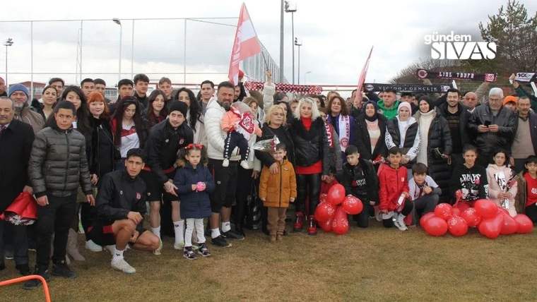 Saha kenarında kırmızı-beyaz bayraklar ve balonlar taşıyan, birlikte poz veren kalabalık grup