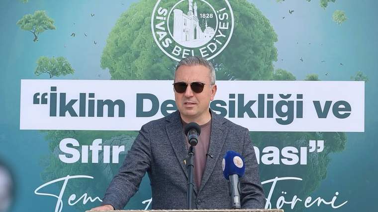 Sivas Belediyesi logolu pankart önünde, kürsüde konuşan bir kişi ve iki mikrofon görülüyor.
