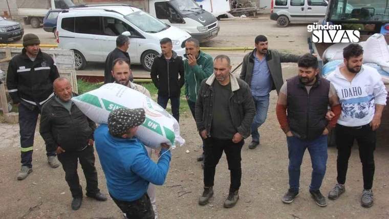 Bir kişi, tohum torbasını omzunda taşırken etrafında birkaç kişi duruyor.
