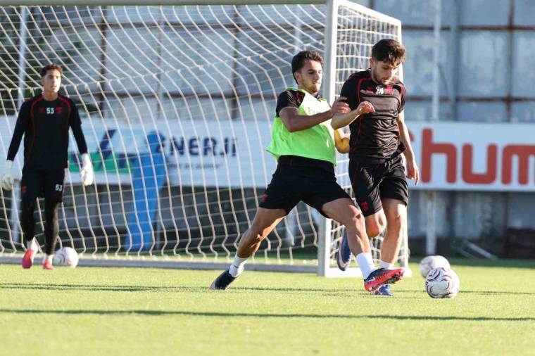 Futbol antrenmanında iki oyuncu top için mücadele ederken, kaleci ve kale ağı da arka planda görülüyor.