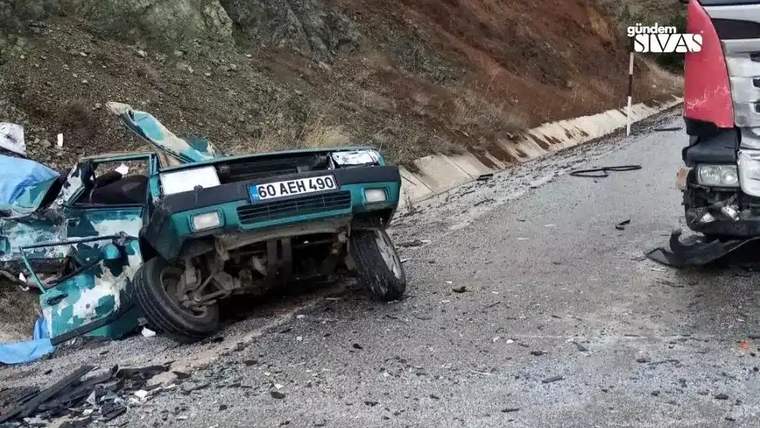 Dağ yolunda önden hasar görmüş otomobil, yanında kısmen görünen tır ve yola saçılmış parçalar bulunuyor.