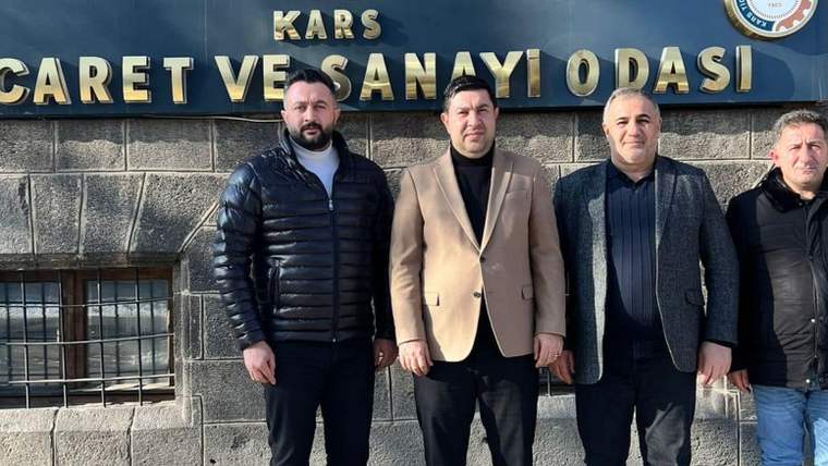 Taş duvarlı bir binanın önünde üç erkek, üzerinde “Kars Ticaret ve Sanayi Odası” yazan tabelanın altında duruyor.