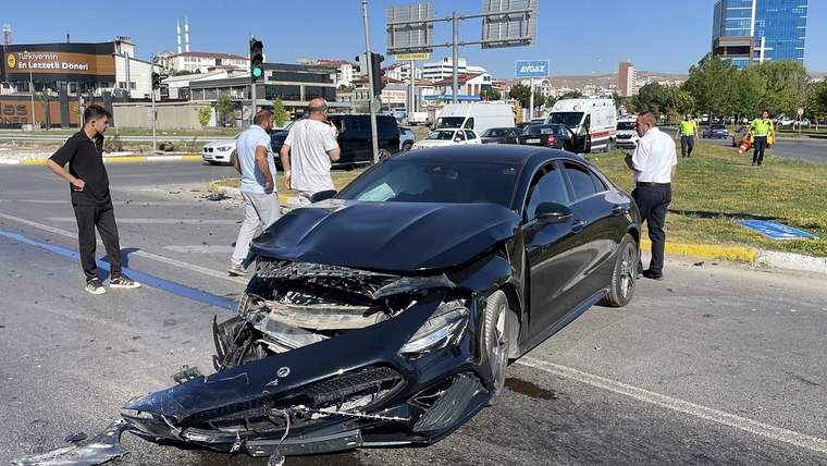 Kavşakta ön kısmı ağır hasar gören siyah sedanın çevresinde birkaç kişi duruyor.