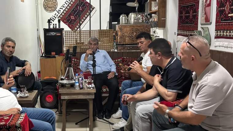Çay içen ve sohbet eden bir grup erkek, geleneksel Türk dekorasyonlu bir mekanda oturuyor.