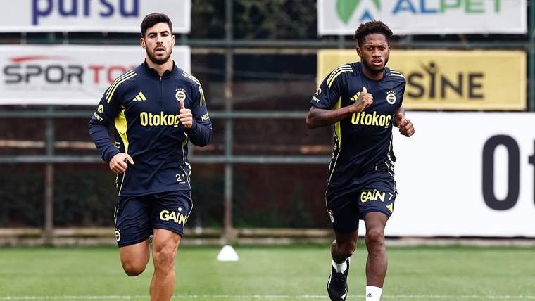 Sarı-lacivert antrenman formaları giyen iki futbolcu, çim sahada yan yana koşuyor.
