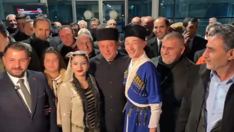 Kars Havalimanı'nda CHP Lideri Özgür Özel ve yanındaki kalabalık, geleneksel kıyafetler giymiş gençlerle poz veriyor.