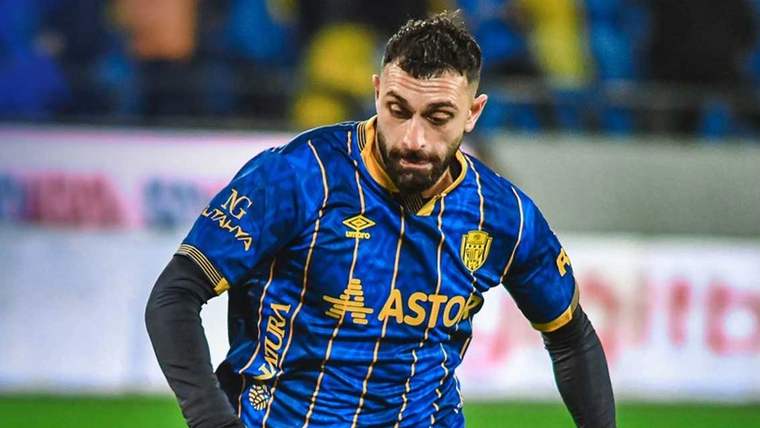 MKE Ankaragücü'nün mavi ve sarı forması giymiş bir futbolcusu, sahada yürürken dikkatle bakıyor.