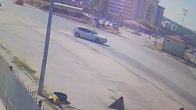 Bir araç, kavşakta drift yaparak ilerliyor. Arka planda binalar ve park halindeki araçlar görünmekte.