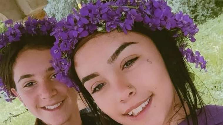İki genç kadın, başlarında çiçeklerle gülümseyerek poz veriyor.