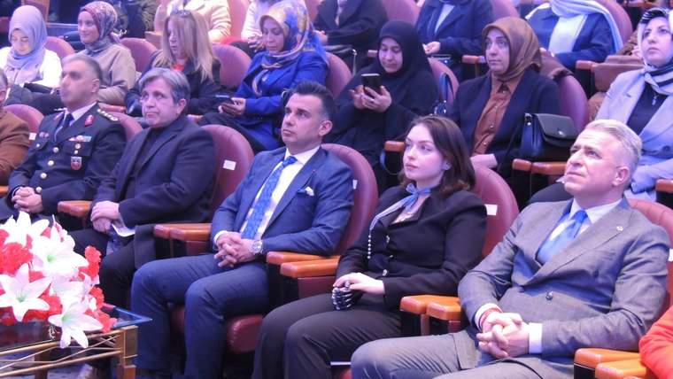 Salon koltuklarında oturan kadın ve erkeklerden oluşan izleyici topluluğu, ön sırada çeşitli kişilerle birlikte görülüyor.
