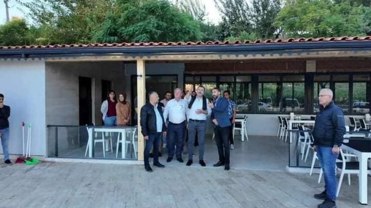 Halk lokantasının önünde bir grup insan, lokantanın açılışı için toplanmış.